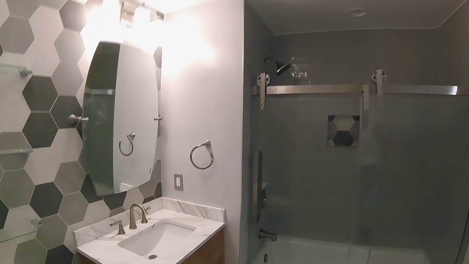 Bathroom remodel with hex accent tile, vanity, and glass tub-shower enclosure